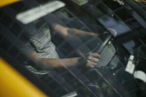 Through glass of windshield of ethnic crop male driver in cab while working in city