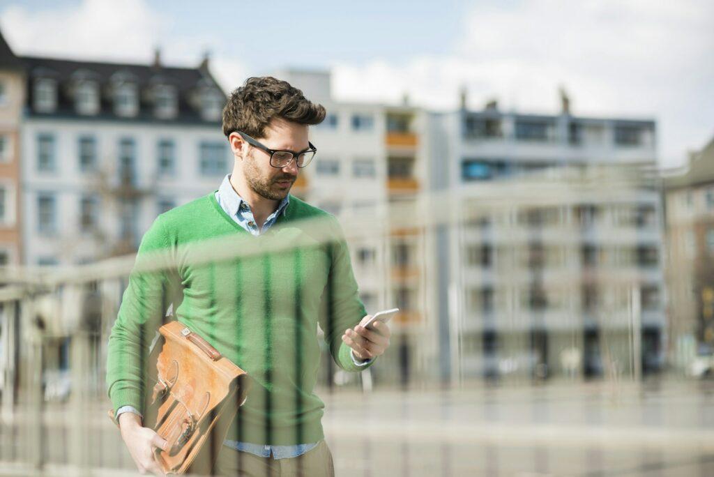 Man in green sweater carrying briefcase, reading text message