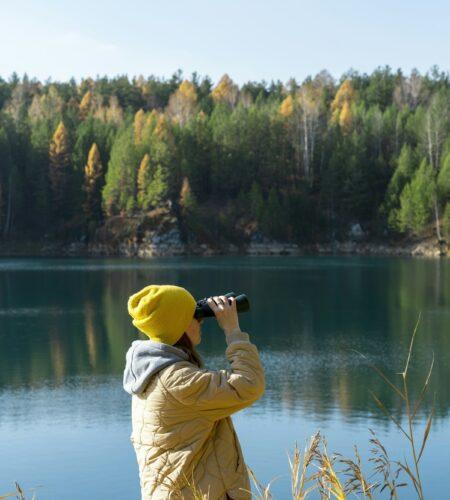 Young woman looking through binoculars at birds on lake ecologist or wild manager , birdwatching