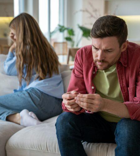 Frustrated spouses ignoring each other after quarrel manipulating silence sitting on sofa at home.